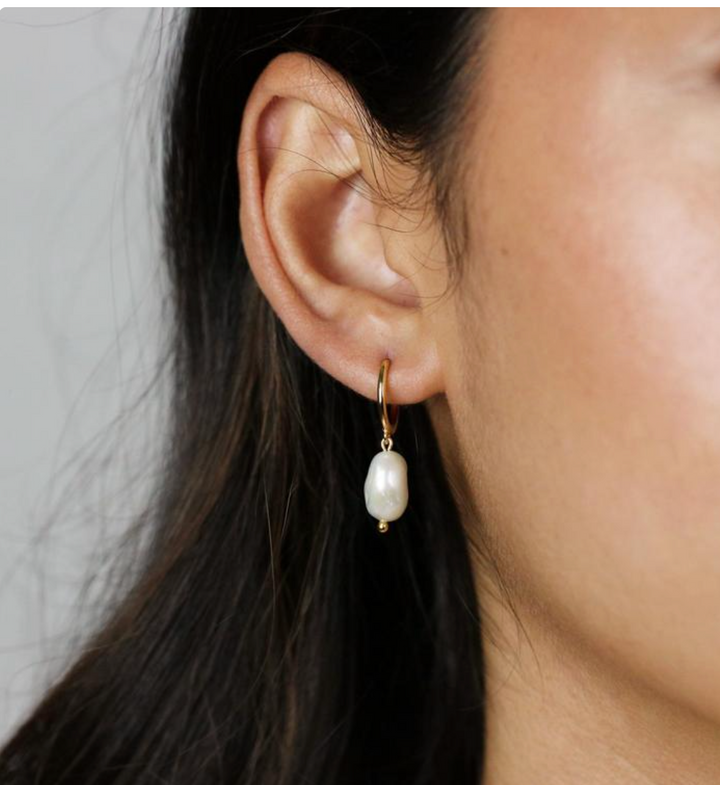 Olivia le model wearing gold hoop earrings with fresh water pearl charms dangling from hoop earring